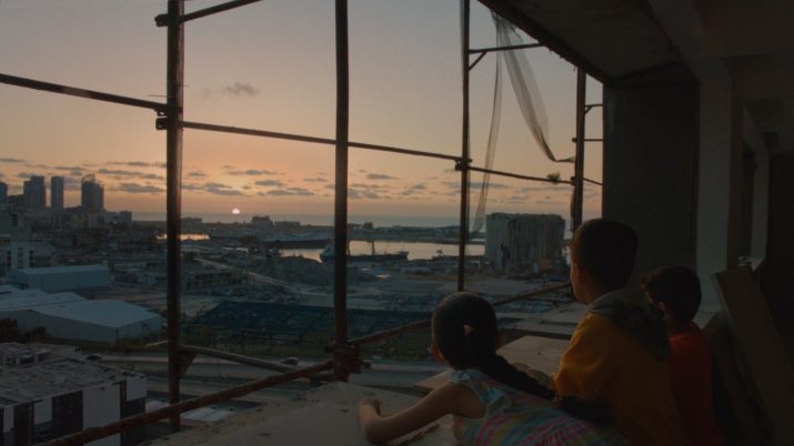 Drei Kinder sind auf einem Hausdach und blicken auf das brennende Hafensilos in der Ferne.
