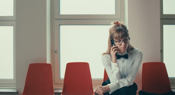 Olga Kosanović sitzt auf einem Stuhl und telefoniert. Filmstill auf NOCH LANGE KEINE LIPIZZANER.