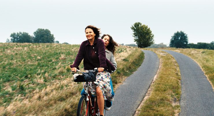 Filmstill aus 'MiroirsNo3' : Zwei Frauen fahren gemeinsam auf einem Fahrrad - ländliche Umgebung