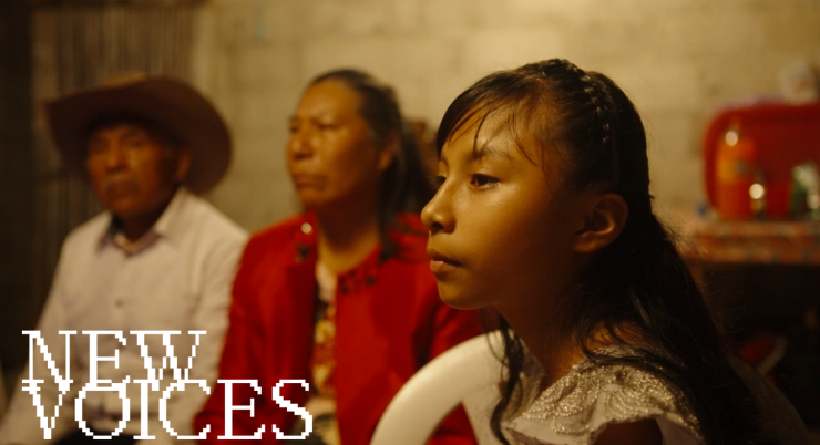 Filmstill aus 'Night of the Coyotes': Ein junges Mädchen sitzt im Vordergrund, zwei ältere Erwachsene sitzen hinter ihr in einem schwach beleuchteten Raum mit kahlen Wänden.