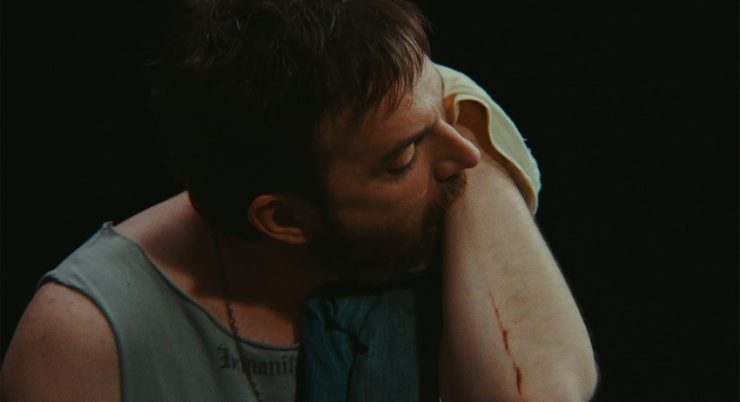 Eine Person vor schwarzem Hintergrund berührt mit dem Mund den eigenen Unterarm.