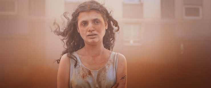 Eine junge Frau mit traurigen Blick ist umgeben und teils bedeckt von beigem Sand.