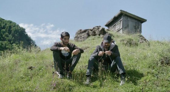 Zwie junge Männer sitzen in der Wiese auf einem Berg.