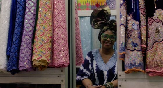 Ein Frau umgeben von bunten Stoffen blickt in den Spiegel.
