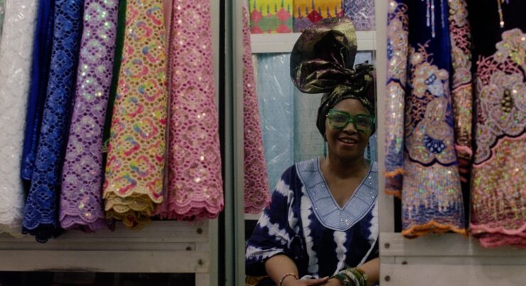 Ein Frau umgeben von bunten Stoffen blickt in den Spiegel.
