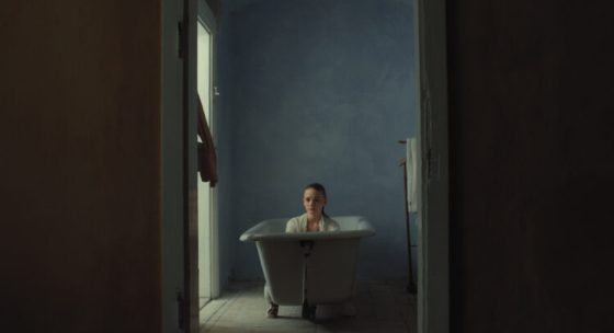 Person sitzt in einer freistehenden Badewanne in einem schmalen, dunklen Raum mit blauer Wand.