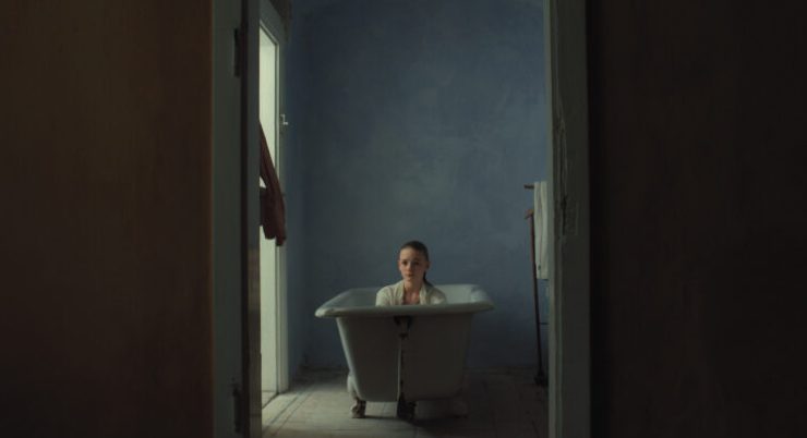 Person sitzt in einer freistehenden Badewanne in einem schmalen, dunklen Raum mit blauer Wand.