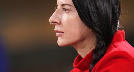 Person mit schwarzem, geflochtenem Haar trägt roten Pullover und sitzt seitlich zur Kamera.