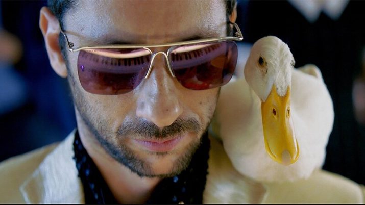 Mann mit Brille und weißem Hemd neben einer weißen Ente mit gelbem Schnabel.