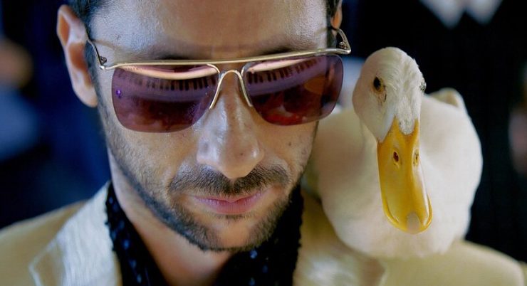 Mann mit Brille und weißem Hemd neben einer weißen Ente mit gelbem Schnabel.