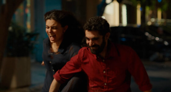 Zwei Personen rennen nebeneinander auf einer Straße in der Nacht, eine Person trägt ein rotes Hemd, die andere ein dunkles Oberteil