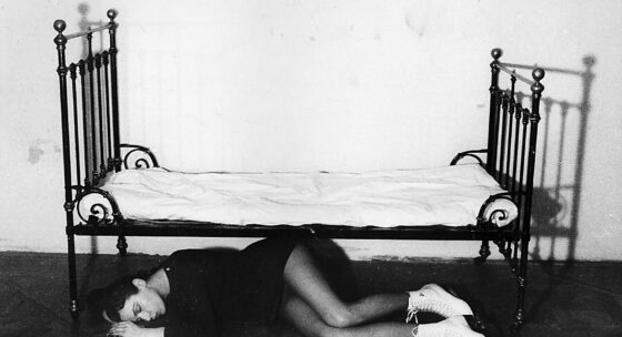 Frau liegt seitlich auf dem Boden unter einem schmiedeeisernen Bett mit weißen Schnürstiefeln