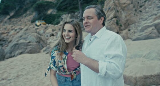 Paar steht am felsigen Strand mit Meer im Hintergrund und einem gelben Auto auf den Felsen