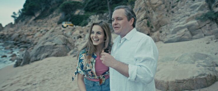 Paar steht am felsigen Strand mit Meer im Hintergrund und einem gelben Auto auf den Felsen