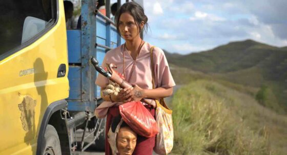 Eine Frau steht neben einen Lastwagen und hat eine Maske sowie einen