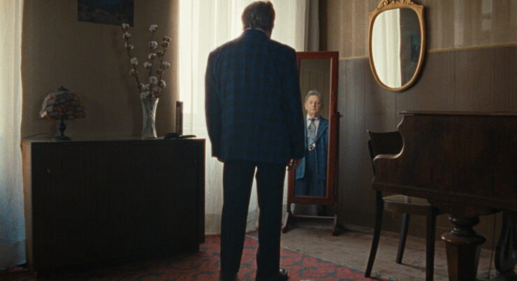 Filmstill: Ein Mann im Anzug blickt zu einem Spiegel