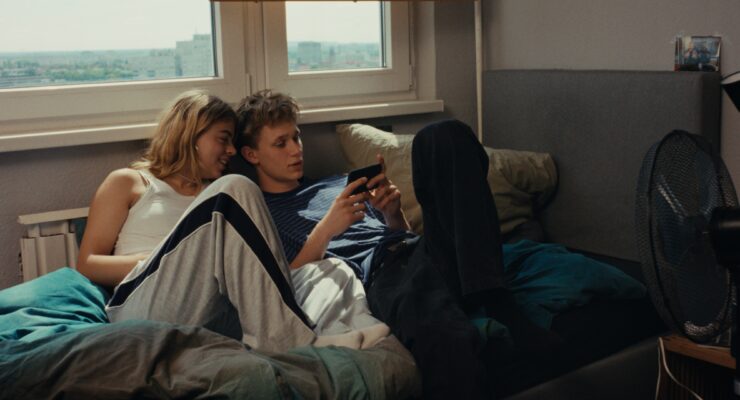 Zwei junge Personen liegen auf der Couch und blicken in ein Handy.