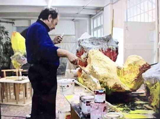 Ein Mann in einem blauen Overall steht neben einem gelben Kunstwerk
